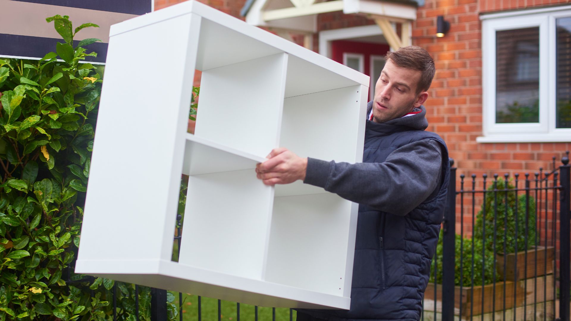 A man holding a white box in front of a house